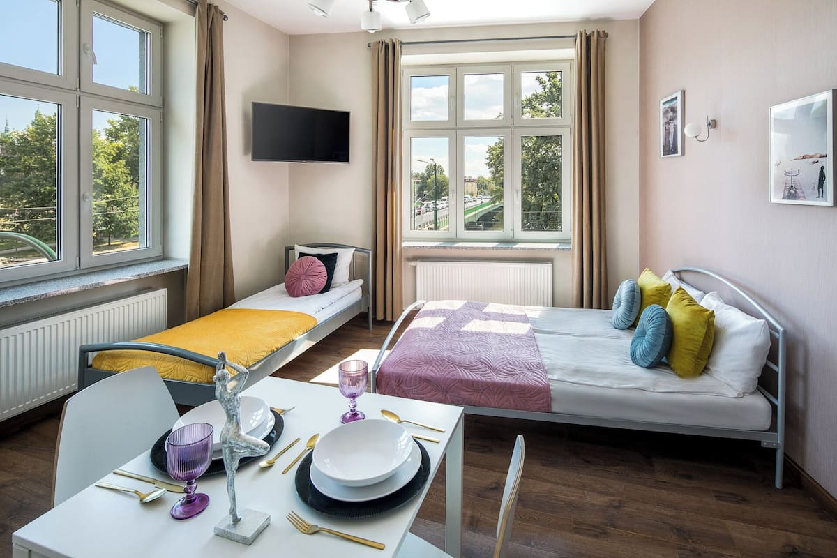 A modern hotel room with a bed, a desk with dining set, and a TV.
