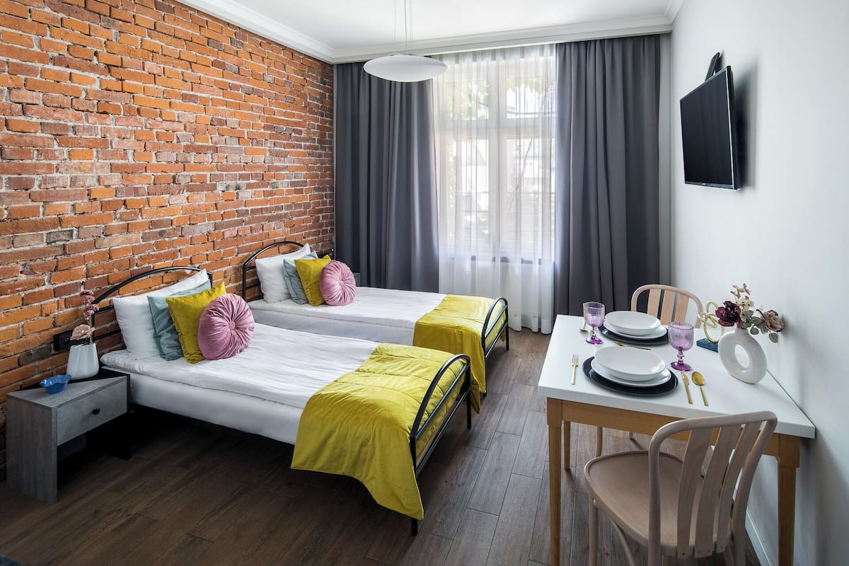A room with two beds, a dining table with chairs, a TV, and a brick wall.