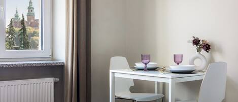Una habitación de hotel con cama, una mesa de comedor con sillas, un florero con flores y vistas a la ciudad a través de una ventana.