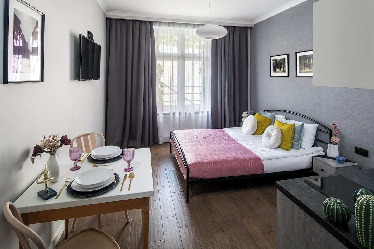 A modern hotel room with a bed, bedside table, and a dining area with a table set for two.