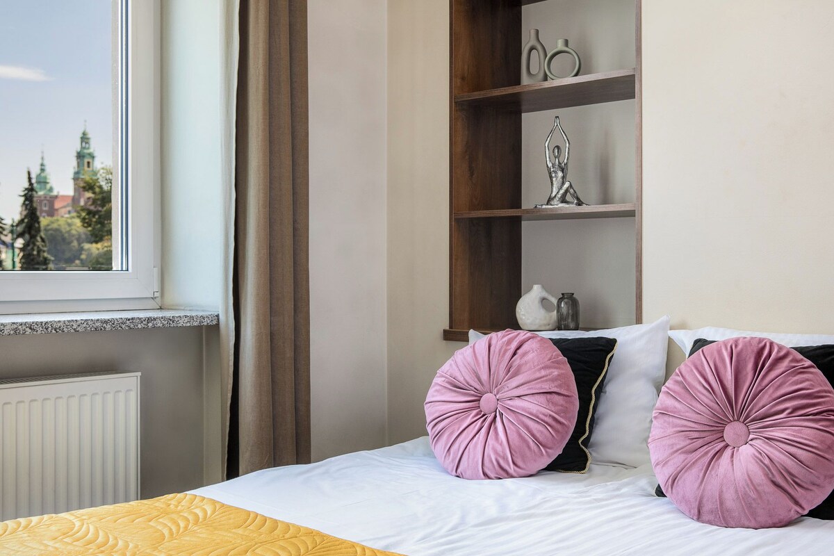 A hotel room with a bed, a window with curtains, a radiator, and a shelf with decorative items.