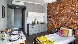 Una camera d'albergo moderna con parete in mattoni, un letto con copriletto giallo e bianco, un angolo cottura e un'area pranzo con tavolo apparecchiato per due.