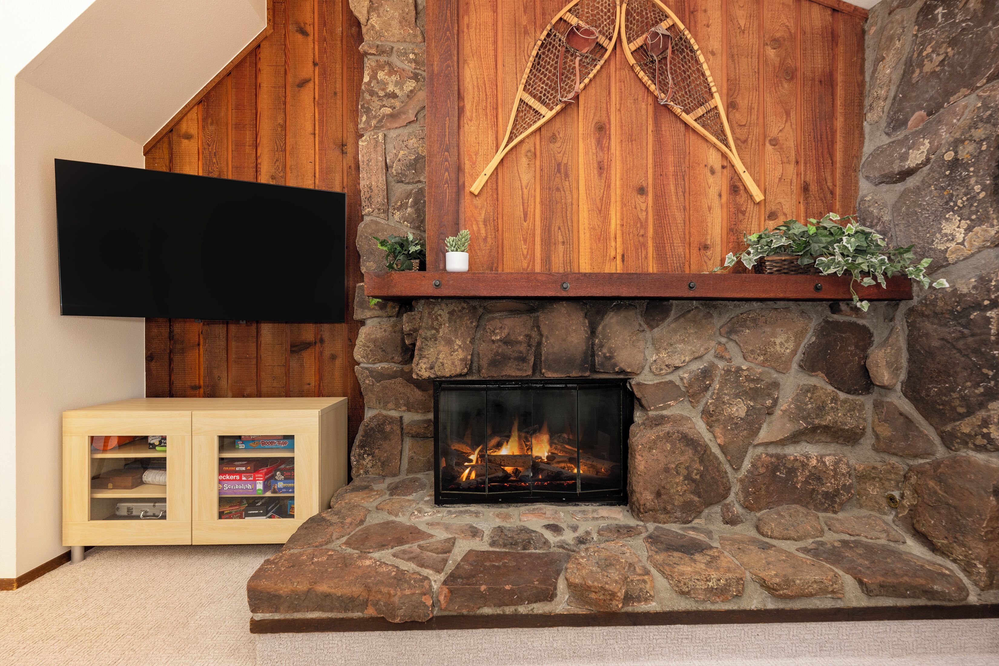 Une cheminée en pierre avec un feu, une étagère en bois au-dessus et un téléviseur fixé au mur.