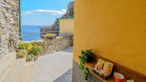 Eine Steintreppe führt zu einem Balkon mit Blick auf das Meer, mit Topfpflanzen und Snacks auf einem Regal.