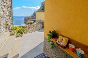 Eine Steintreppe führt zu einem Balkon mit Blick auf das Meer, mit Topfpflanzen und Snacks auf einem Regal.