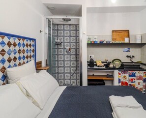 Ein Hotelzimmer mit einem Bett, einer Dusche, einer kleinen Küchenzeile und einem Badezimmer mit gemusterten Fliesen.
