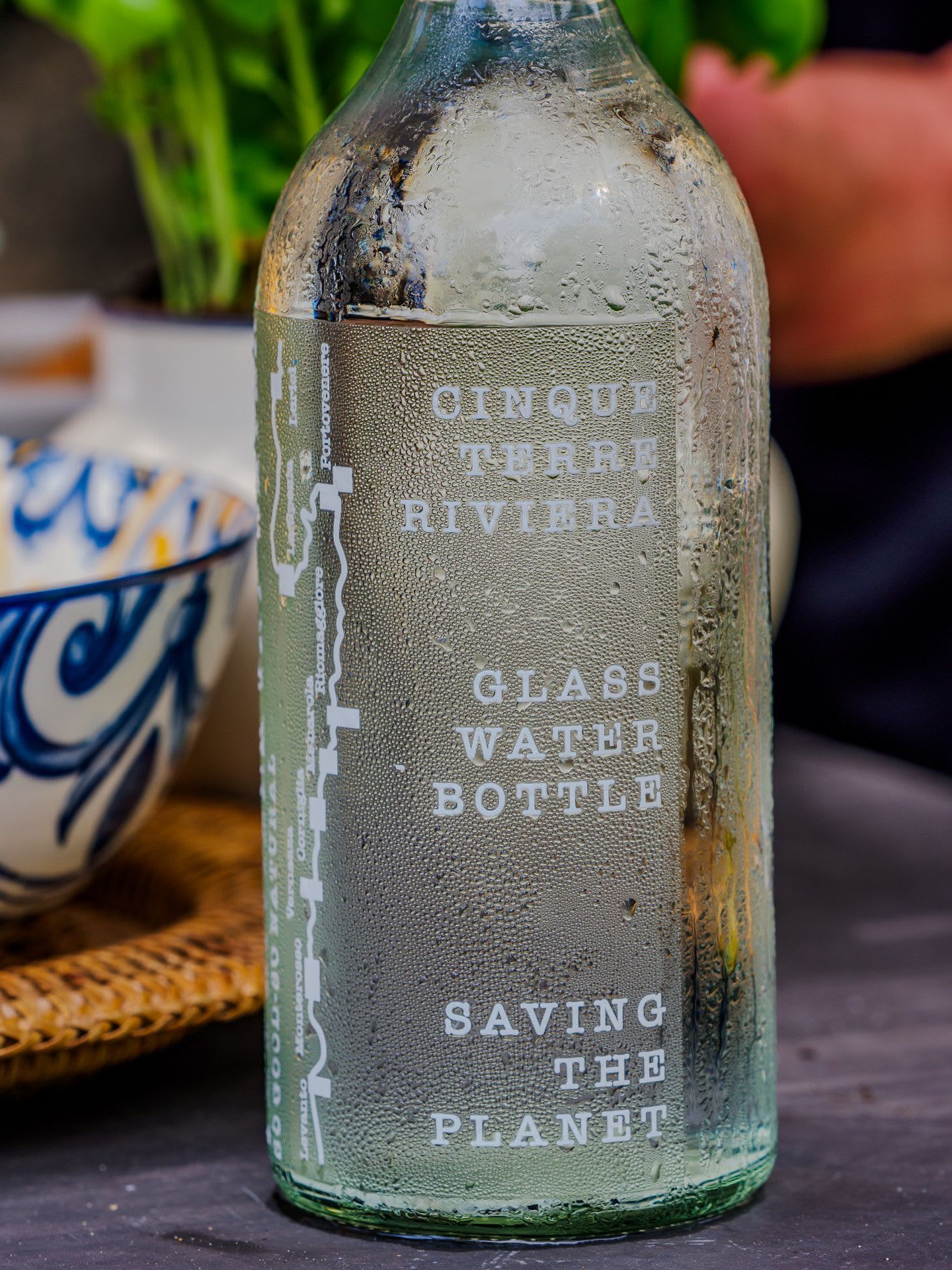 A glass bottle with embossed text, placed on a surface with a bowl and a basket in the background.