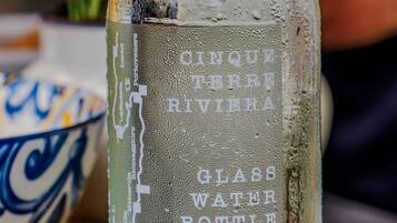 A glass bottle with embossed text, placed on a surface with a bowl and a basket in the background.