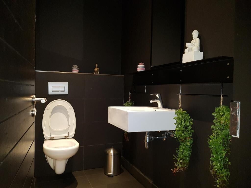 A modern bathroom with a white toilet, a white sink, and a black wall.