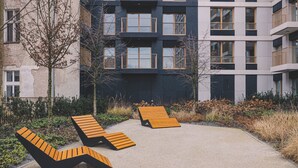 A modern building with multiple balconies, a paved area with lounge chairs, and a garden with shrubs and trees. - Rosa - Obud si w Sercu pi Knej Bydgoszczy (Bydgoszcz)