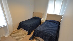 A room with two single beds, a bedside table with a lamp, and a window with curtains.