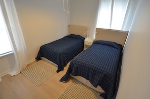 A room with two single beds, a bedside table with a lamp, and a window with curtains.