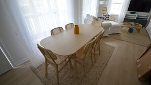 A dining area with a table and chairs, a sofa, a television, and a window with curtains.
