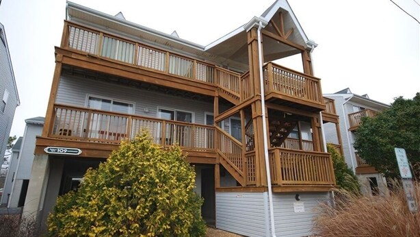 A multi-story residential building with a wooden balcony and a small tree in front.