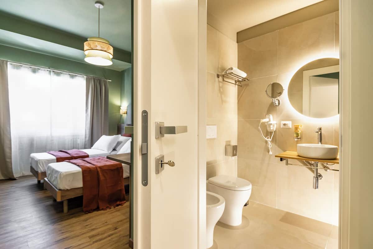 A hotel room with two beds, a bathroom with a toilet, sink, and mirror.
