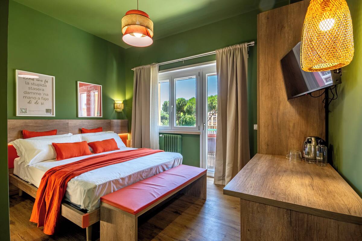 A bedroom with a bed, a bench, a TV, and a window with curtains.