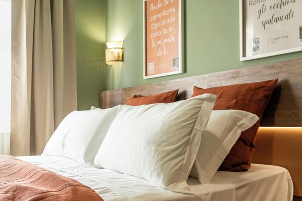A neatly made bed with white and brown pillows, a wooden headboard, and a wall with framed text and a wall-mounted light fixture.
