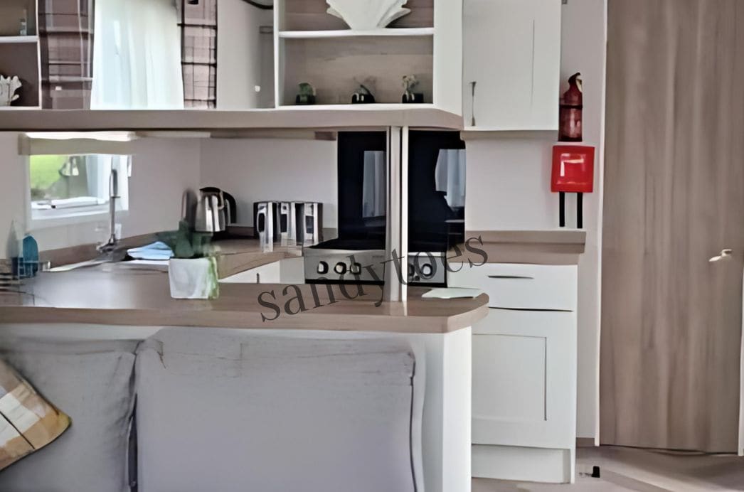 A modern kitchen with white cabinets, a countertop, and a sink. There is a red fire alarm on the wall.