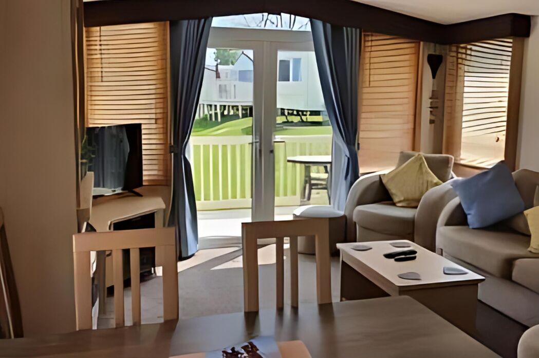A cozy living area with a sofa, a coffee table, and a TV. There is a sliding glass door leading to a balcony with a table and chairs.
