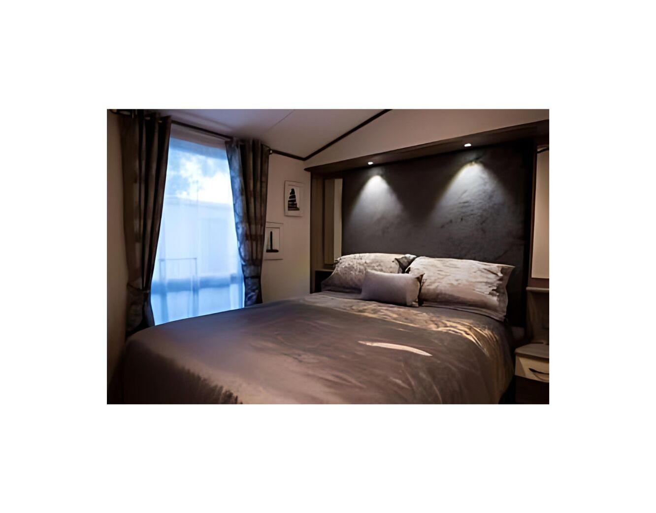 Un dormitorio moderno con una cama grande, una mesita de noche, una ventana con cortinas y un aplique de pared.