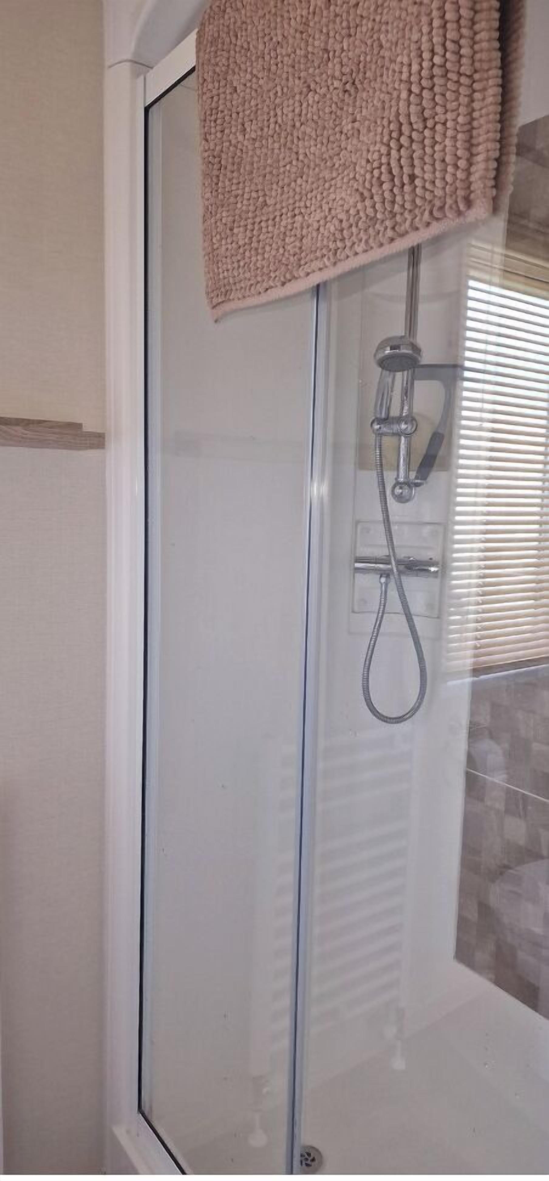 Un espace douche clos par des parois de verre, équipé d’un pommeau de douche à main et d’un porte-serviettes.