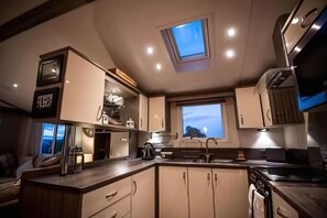 A compact kitchen with a skylight, built-in appliances, and a view of the outdoors. - Sandytoes Holidays (Paignton)