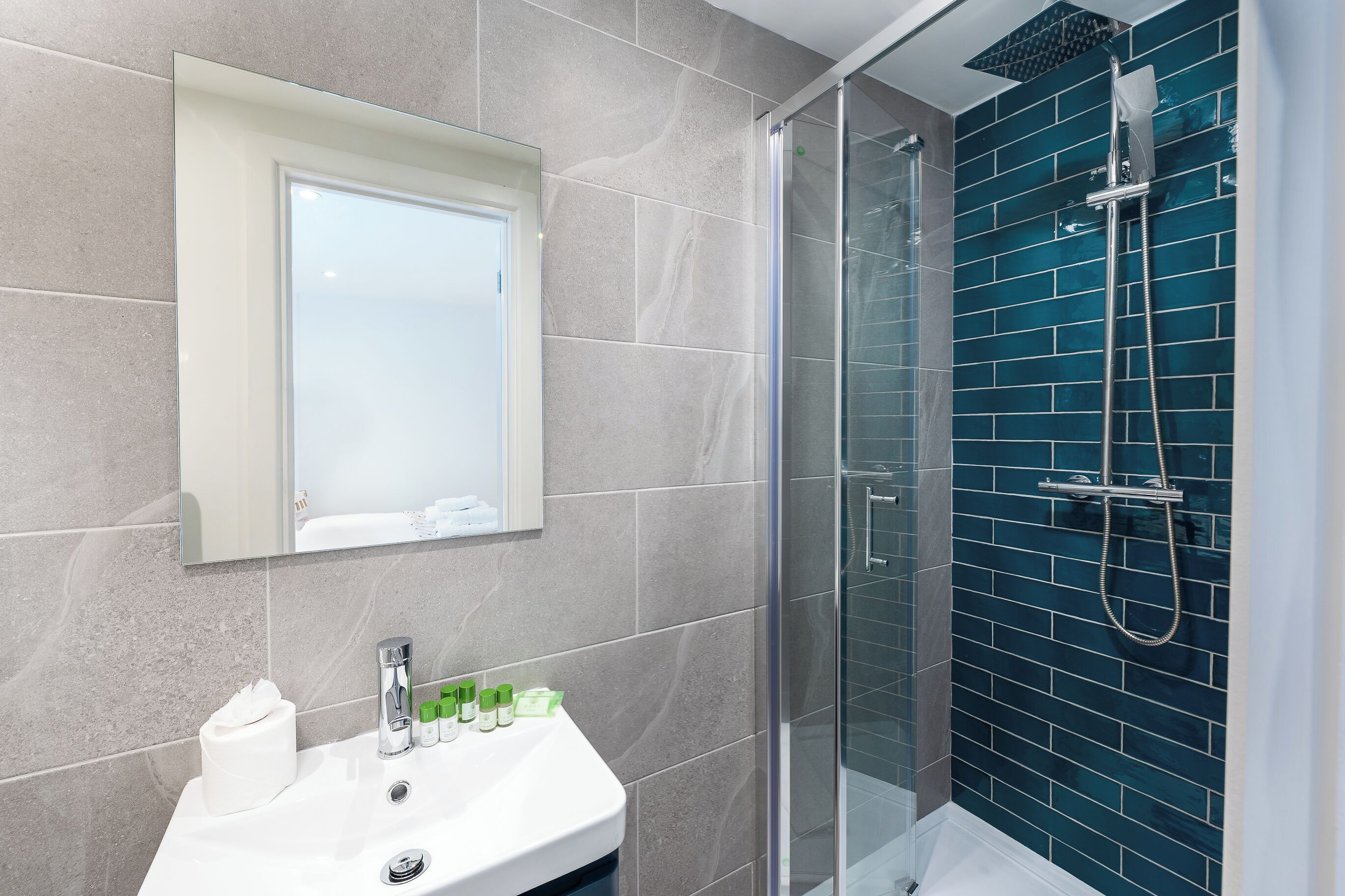 A bathroom with a glass-enclosed shower, a sink with toiletries, and a mirror.