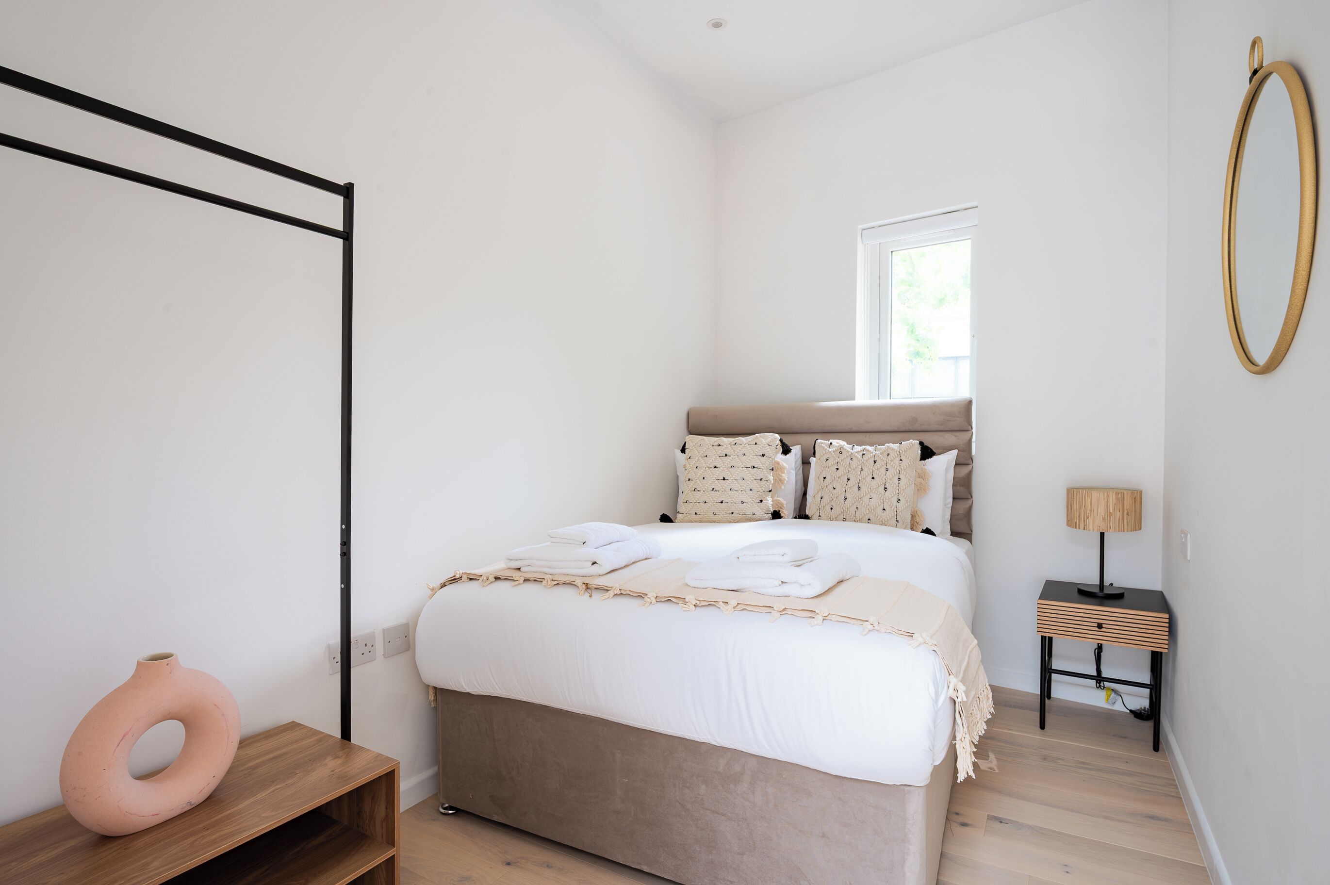 A bedroom with a bed, bedside table, lamp, and a large mirror on the wall.