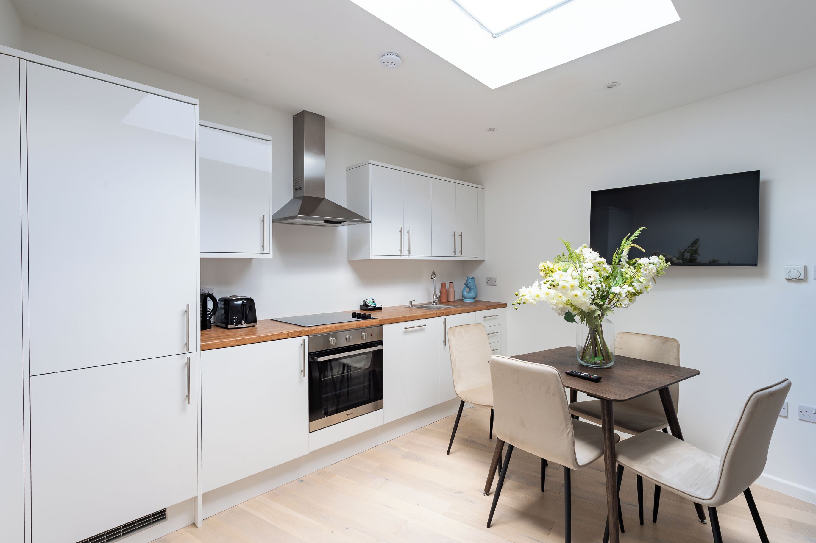 A modern kitchen with white cabinets, a wooden countertop, a built-in oven, and a skylight.