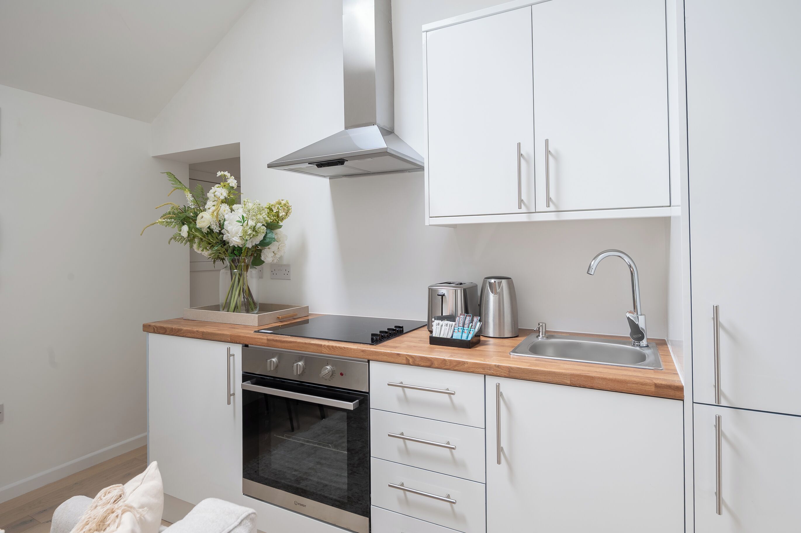A modern kitchen with white cabinets, a stainless steel range, a built-in oven, a wooden countertop, and a vase with flowers.