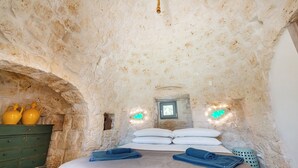 Une pièce rustique aux murs de pierre, avec un lit, des oreillers et une commode verte.