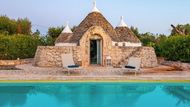 Un bâtiment en pierre surmonté d’un toit conique, avec une piscine et deux chaises longues.