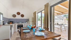 Un coin repas avec une table en bois dressée pour quatre personnes, une cuisine avec un dosseret décoré, et une vue sur le patio extérieur.