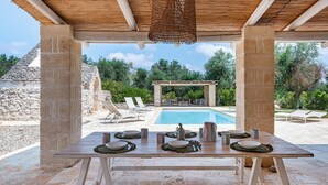Une table en bois, dressée pour le repas, avec une piscine et des chaises longues en arrière-plan.