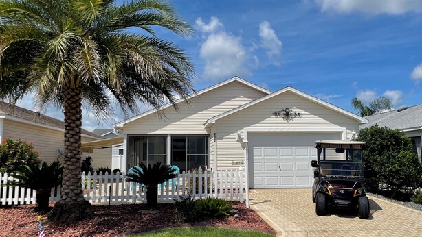 A residential house with a garage, a palm tree, and a golf cart parked in front. - Modern charm meets vibrant living with outdoor oasis and golf cart fun! (The Villages)
