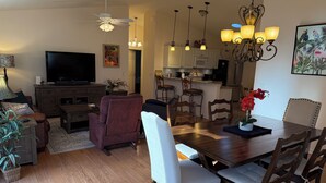 A modern living room with a flat-screen TV, a ceiling fan, and a dining area with a wooden table and chairs. - Modern charm meets vibrant living with outdoor oasis and golf cart fun! (The Villages)