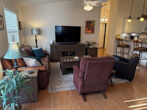 A living room with a TV, sofa, armchair, coffee table, lamp, and a potted plant.