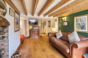 Uma sala de estar aconchegante com sofá de couro, vigas de madeira, lareira de tijolos e uma televisão.