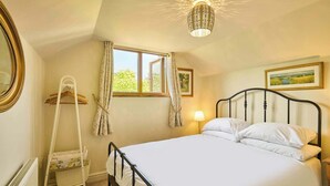 A bedroom with a bed, a radiator, a window with curtains, a hanging lamp, and a framed picture on the wall. - Host & Stay | Romney Cottage (Corpusty)