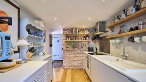 A modern kitchen with white cabinetry, a brick wall, and various kitchen utensils and appliances. - Host & Stay | Romney Cottage (Corpusty)