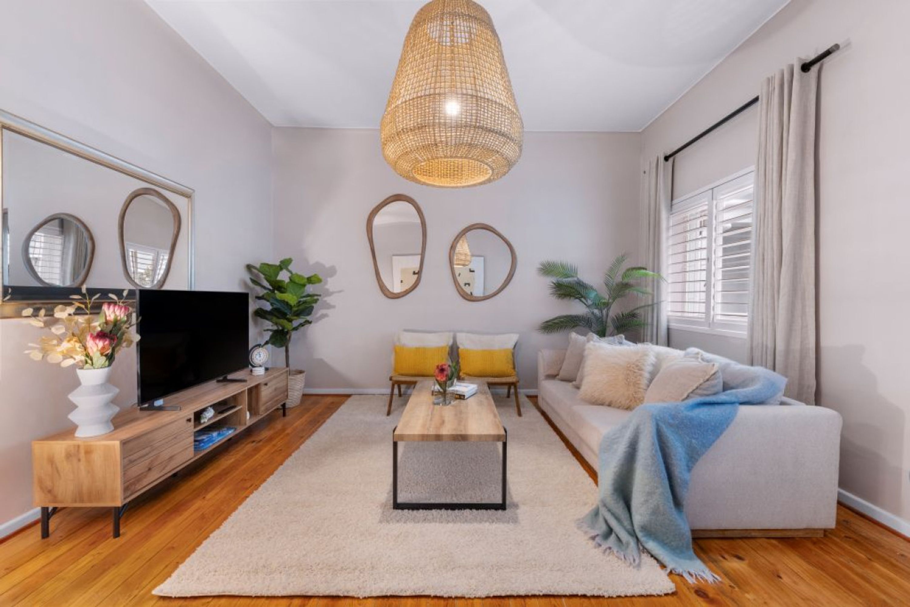 Een moderne woonkamer met een flatscreen televisie, een houten entertainmentkast, een bijzettafeltje, een bank en een grote geweven hanglamp.