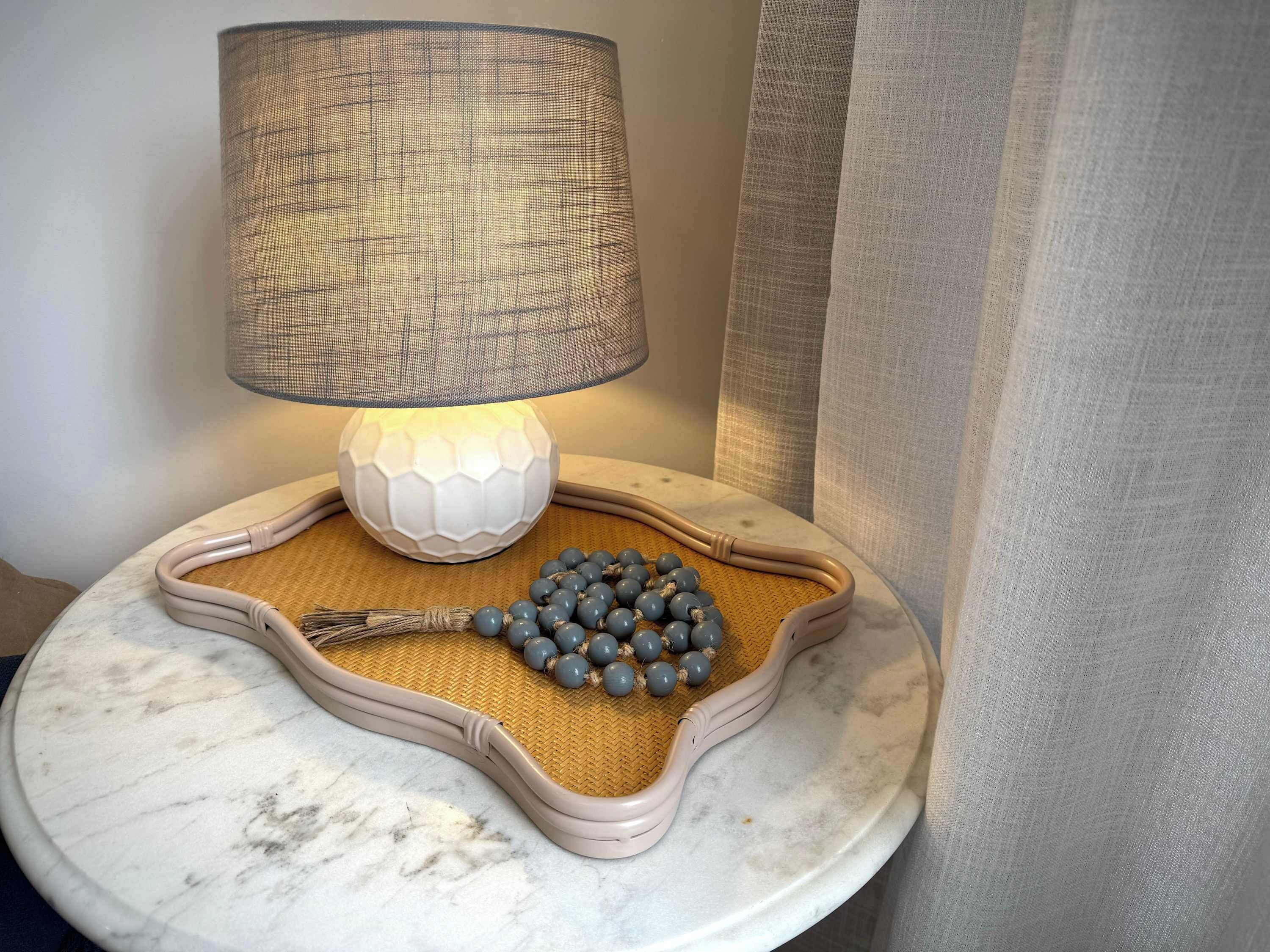 A table with a lamp, a woven tray, and a bunch of grapes.