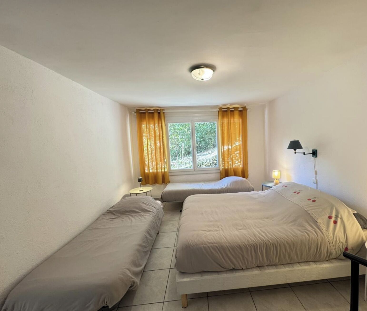 Een kamer met twee bedden, een raam met gordijnen, een nachtkastje met een lamp en een wandlamp.