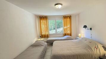 Een kamer met twee bedden, een raam met gordijnen, een nachtkastje met een lamp en een wandlamp.