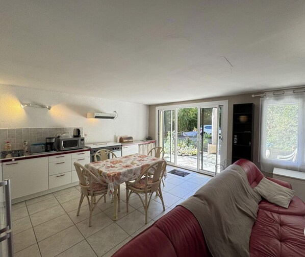 A compact kitchen with a dining table and chairs, a red sofa, and a sliding glass door leading to a patio.