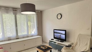 Un salon avec un téléviseur, une horloge, une fenêtre avec des rideaux et un canapé.