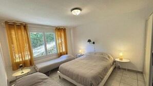 Une chambre avec deux lits, une fenêtre avec des rideaux, une table de chevet avec une lampe et une lampe fixée au mur.