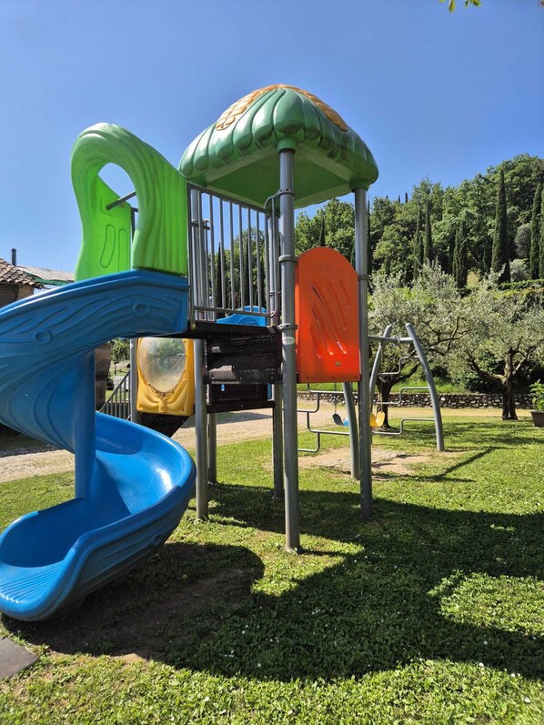 A playground with a blue slide, a green climbing structure, and an orange climbing frame. - Locanda Cà del Ponte (Costermano sul Garda)