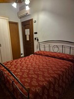 Una camera da letto con un letto, una porta in legno, un condizionatore d'aria e un tavolino con una sedia.