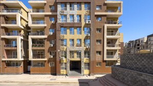 A multi-story residential building with balconies, air conditioning units, and a central entrance.